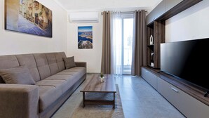 A modern living room with a sofa, coffee table, TV, and artwork on the walls. - Luxury 1BR Stay at The Podium - Marina (Msida)