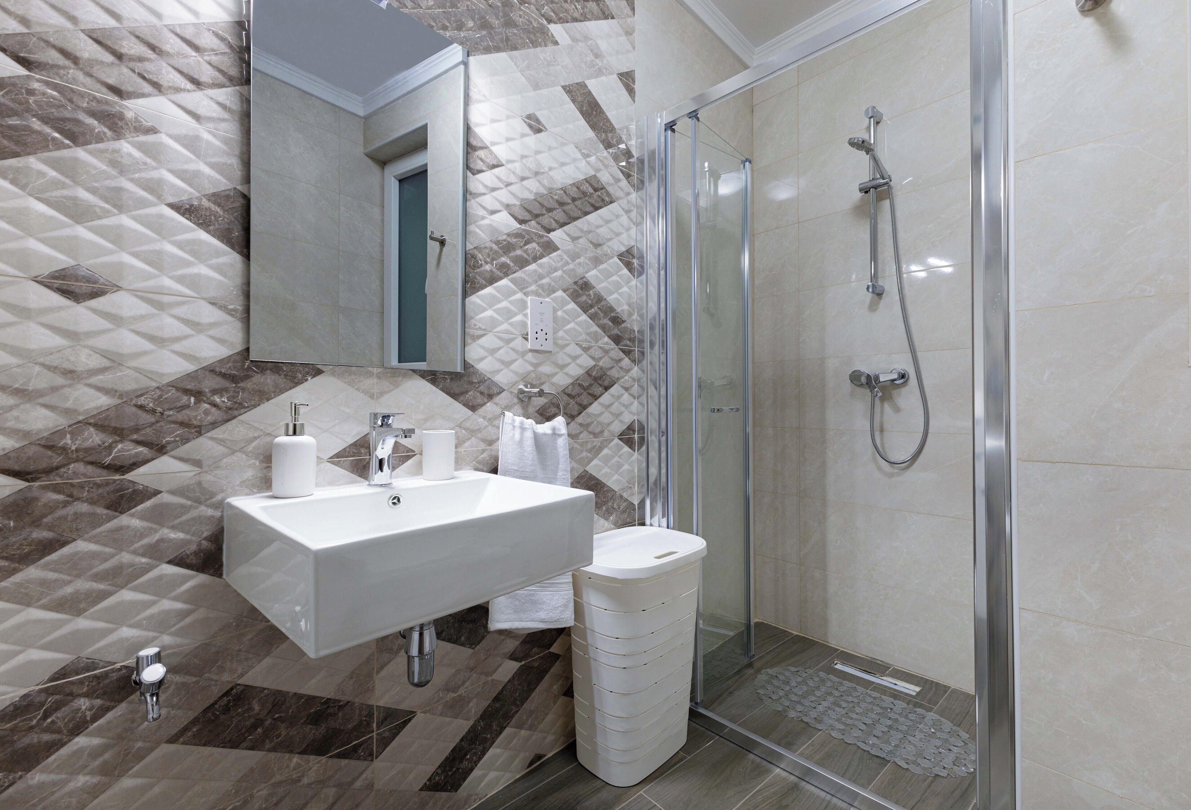 A modern bathroom with a glass-enclosed shower, a white sink, and a patterned tile backsplash.