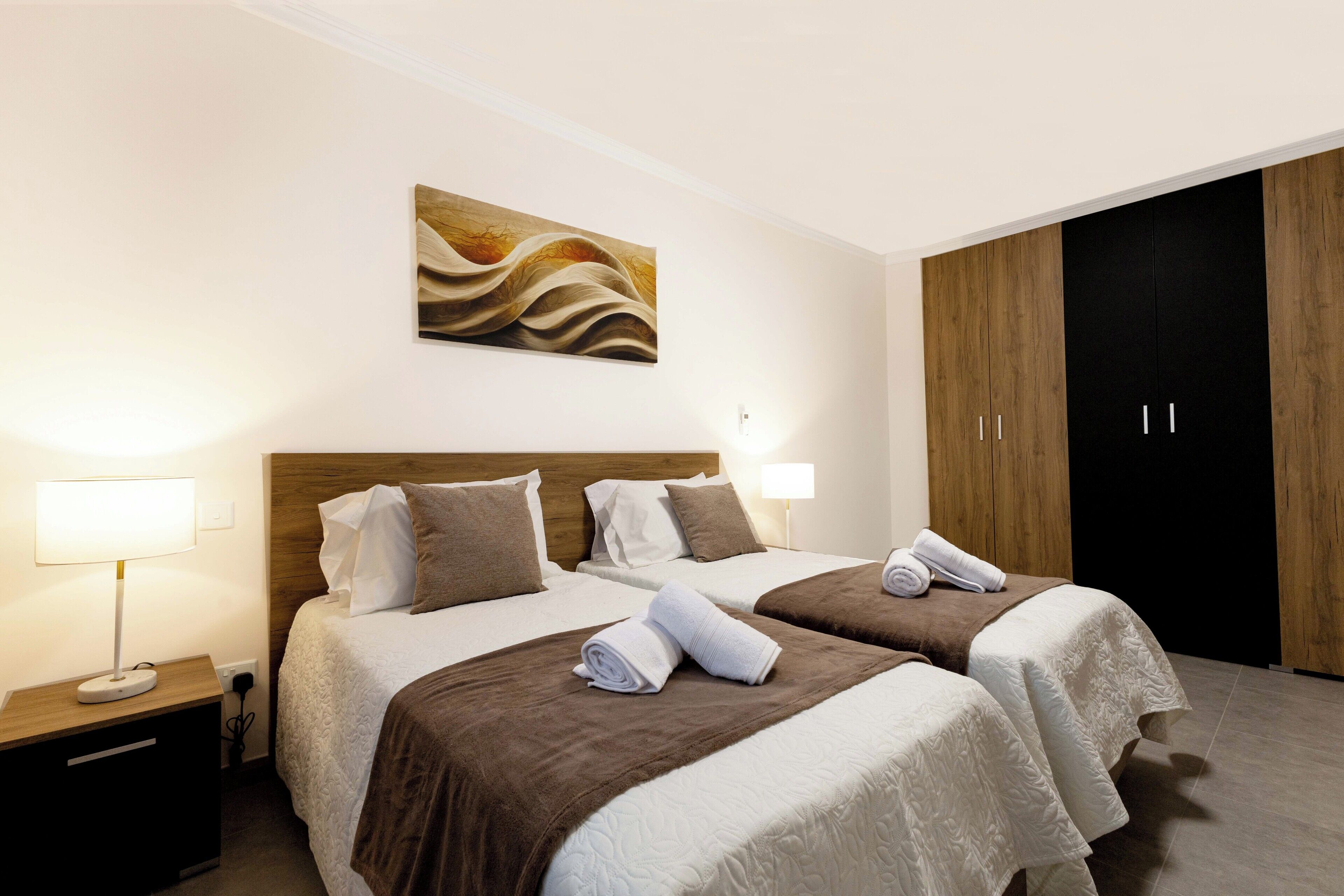 Une chambre d’hôtel avec deux lits, un tableau au mur, une armoire et une table de chevet avec une lampe.
