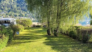 Un'area verde ben curata con un cartello segnaletico, alberi e vista su un lago e edifici sullo sfondo.