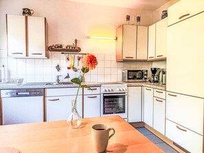 A kitchen with white cabinets, a microwave, an oven, a sink, and a vase with a flower on the counter.