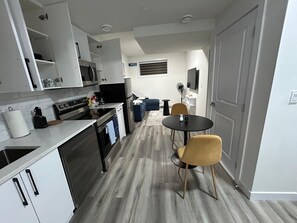 Een compacte keuken met moderne apparatuur, een zithoek met twee stoelen en een flatscreen televisie aan de muur.