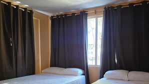 Une chambre avec deux lits, une fenêtre avec des rideaux et un sol carrelé.