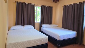 Deux lits simples avec du linge de lit blanc, une fenêtre avec des rideaux et une structure de plafond en bois.
