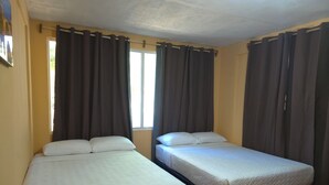 Deux lits simples avec des têtes de lit, une fenêtre avec des rideaux et un mur jaune uni.