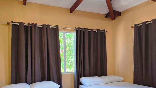 Une chambre avec deux lits, une fenêtre avec des rideaux et un sol carrelé.