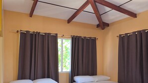 Une chambre avec deux lits, une fenêtre avec des rideaux, un sol carrelé et un plafond en pente avec des poutres en bois.