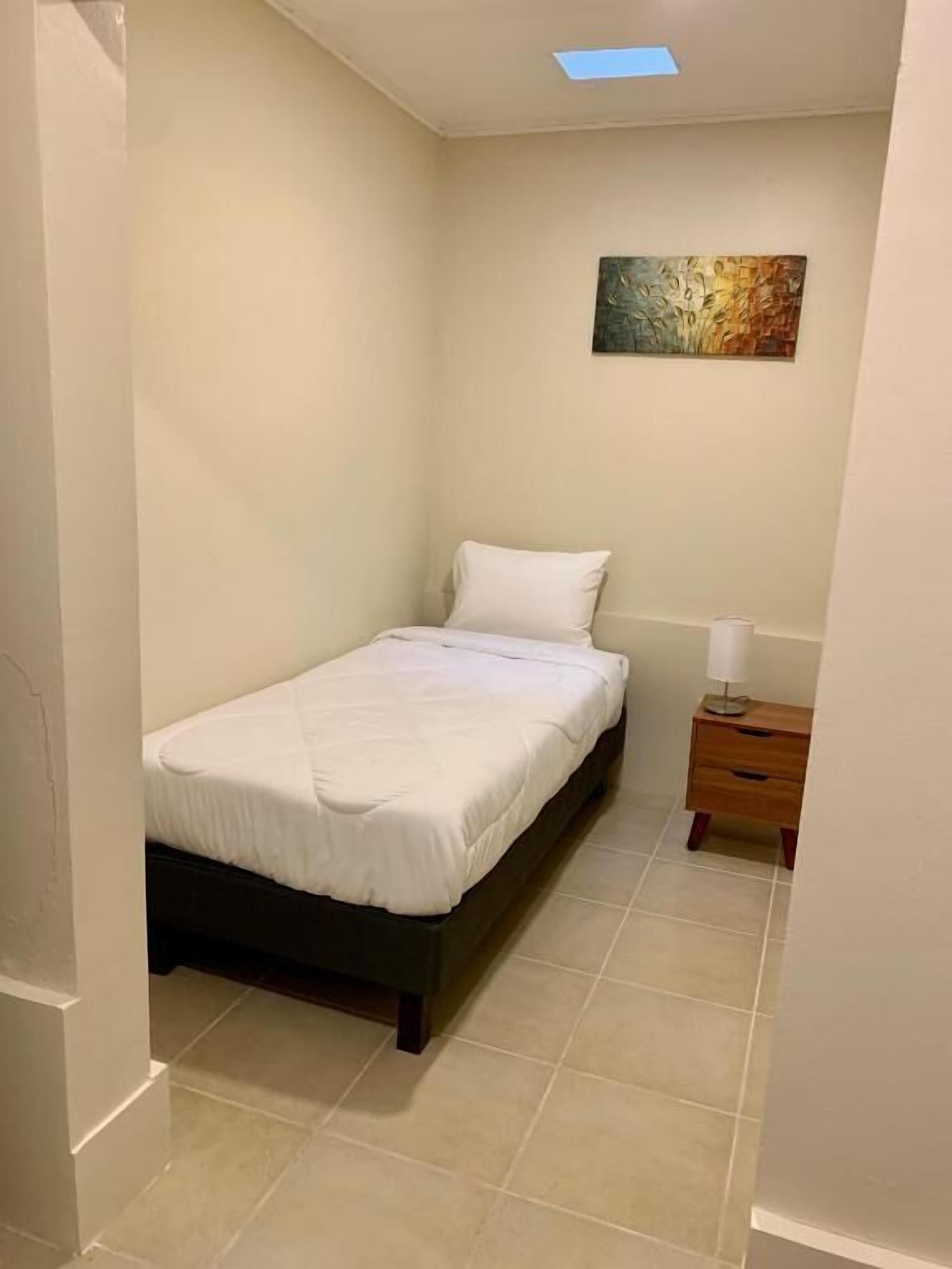 A small, clean bedroom with a single bed, a nightstand, and a wall-mounted painting.