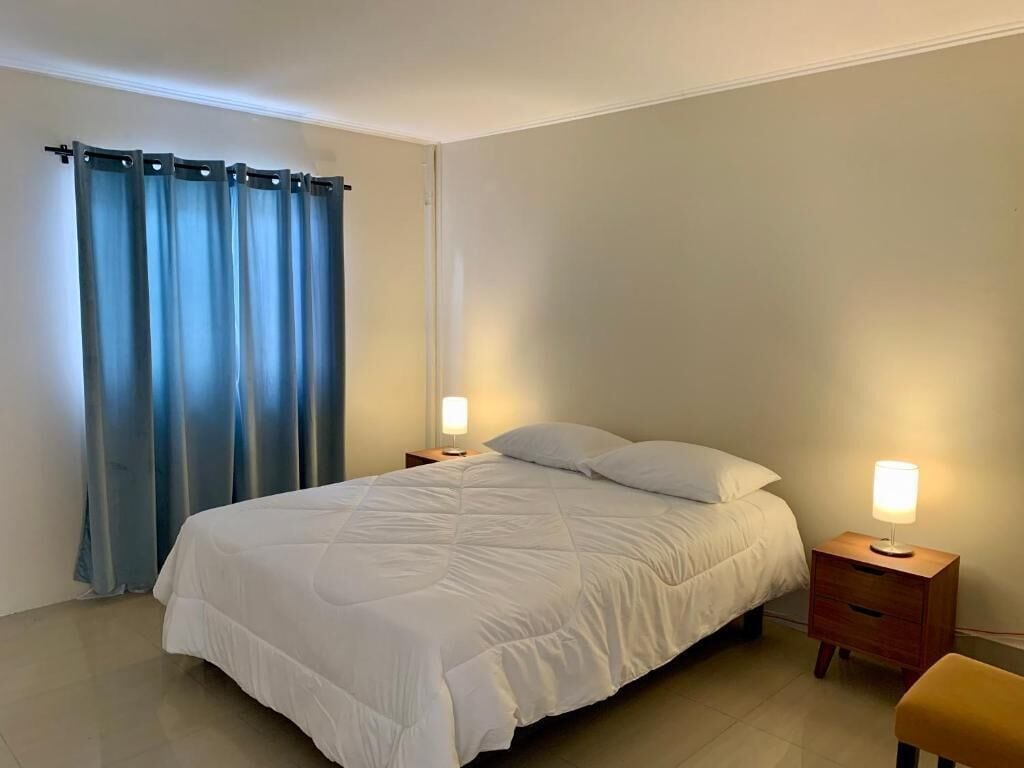 Een slaapkamer met een bed, twee nachtkastjes met lampen, een stoel en een gordijn.