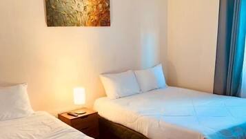 A hotel room with two beds, a nightstand, a lamp, and a painting on the wall.