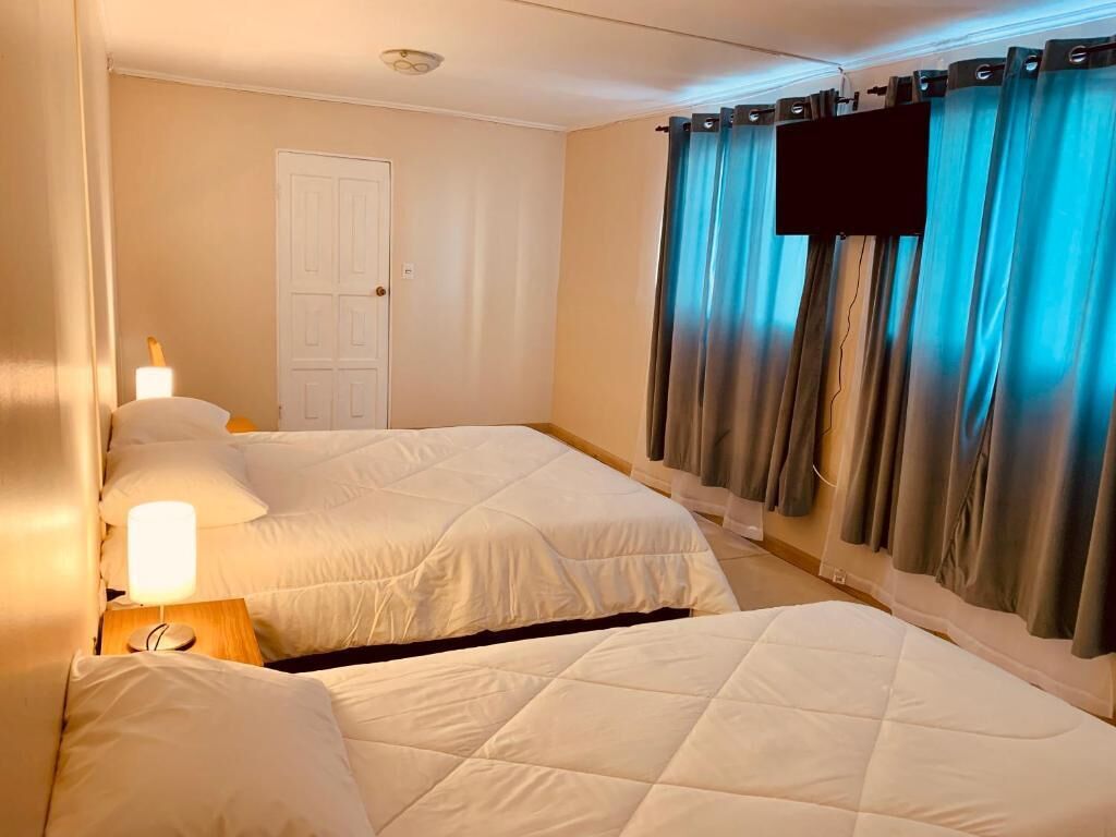 Habitación de hotel con dos camas, una puerta blanca y cortinas azules.