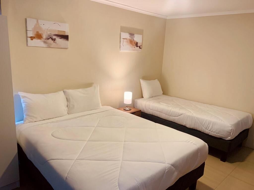 A hotel room with two beds, a nightstand with a lamp, and abstract wall art.