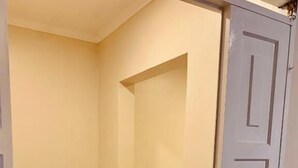 En smal hall med en dörr som leder till ett sovrum med en säng och ett litet fönster.