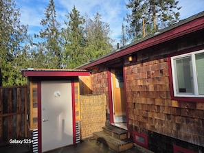 A wooden cabin with a red door, a small attached shed, and a window with blinds.