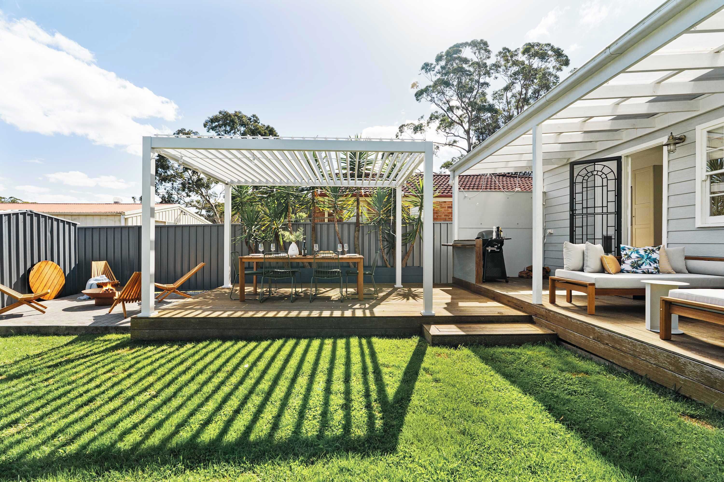 Ein Garten mit Pergola, Essbereich und einer Sitzgruppe inklusive Sofa und Tisch.