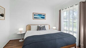 Quarto com cama, abajures, um quadro emoldurado e uma janela com cortinas.
