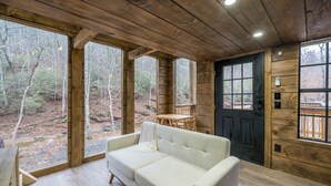 Interior de una cabaña de madera con sofá, una mesa y una puerta.