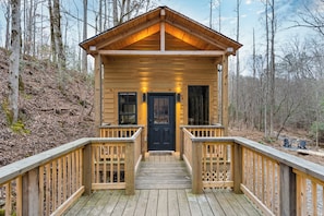 Une cabane en bois avec un porche à l’avant, une porte noire et une petite terrasse.