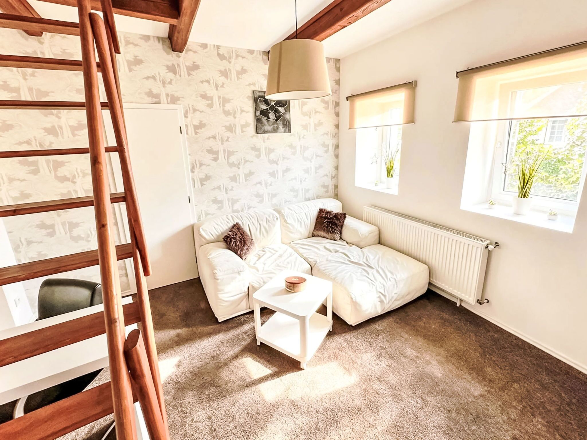 Een knus ingerichte kamer met een witte bank, een klein witte tafel, een houten trapje en een radiator.