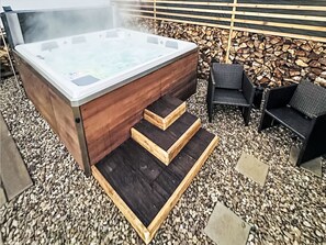 A hot tub with wooden steps leading up to it, surrounded by gravel and black wicker chairs. - Bukanda by Interhome (Mladé Buky)