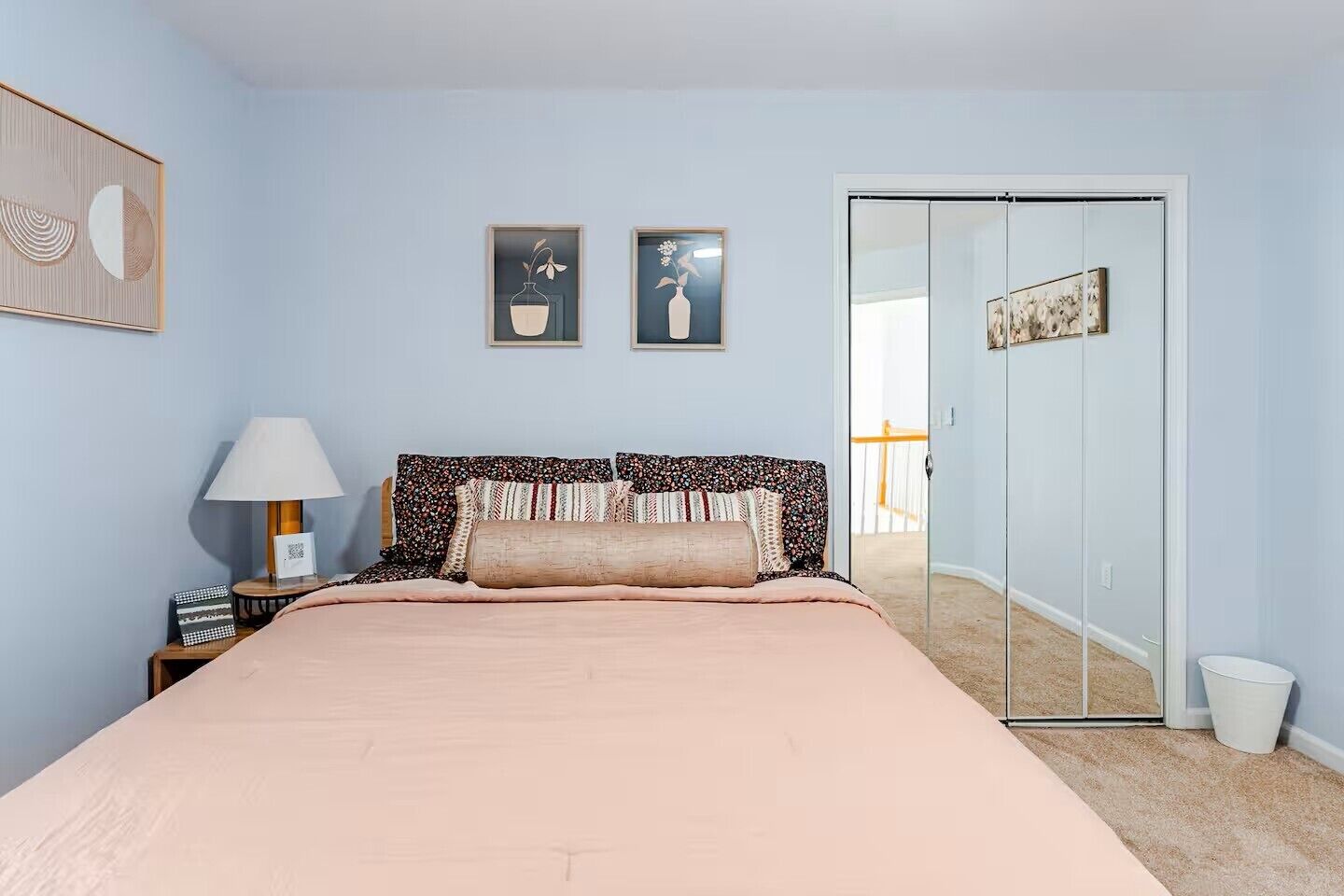 Une chambre à coucher comprenant un lit, une table de chevet, une lampe, deux tableaux encadrés et une porte coulissante donnant sur un balcon.