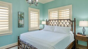 Quarto com cama de madeira, roupa de cama branca, um candelabro e uma mesa de cabeceira com abajur.
