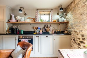 A kitchen with a stone wall, wooden shelves, and a dining area with a chair.