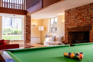 A billiards table in a room with a brick fireplace, a sofa, and a lamp. - Stunning Five Bedroom Home Near Tewkesbury (Forthampton)