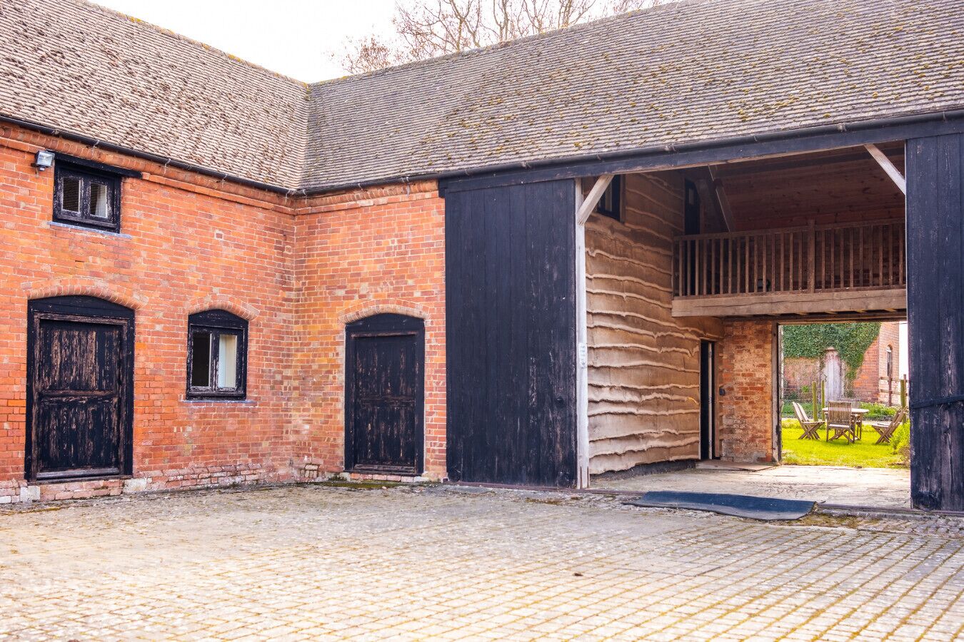 A brick building with three arched windows and a covered outdoor area with a table and chairs.