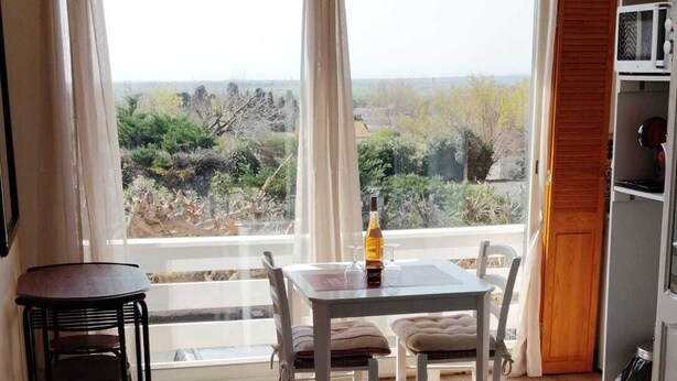 A room with a dining table, chairs, a bottle, and a view of the outdoors. - Bright studio apartment near the beaches – Portiragnes Village (Portiragnes)