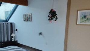 A bedroom with a bed, a bedside table, a hanging plant, a framed picture, and a window with curtains. - Bright studio apartment near the beaches – Portiragnes Village (Portiragnes)