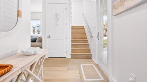 A hallway with a wooden bench, a white door, and a staircase leading to an upper floor. - Spirit of the Ocean 404 RET (Port Aransas)