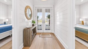 A hallway with white paneled walls, a wooden bench, a mirror, and a door leading outside. - Spirit of the Ocean 404 RET (Port Aransas)