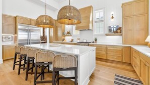 A modern kitchen with a large island, wooden cabinets, and wicker pendant lights. - Always Summer 157 DEW (Port Aransas)