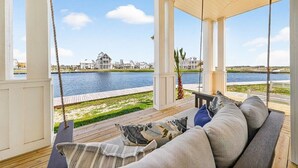A covered outdoor seating area with a view of a water body and buildings in the background. - Always Summer 157 DEW (Port Aransas)