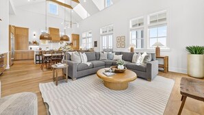 A spacious living area with a large gray sectional sofa, a wooden coffee table, and a dining area with wooden chairs. - Always Summer 157 DEW (Port Aransas)