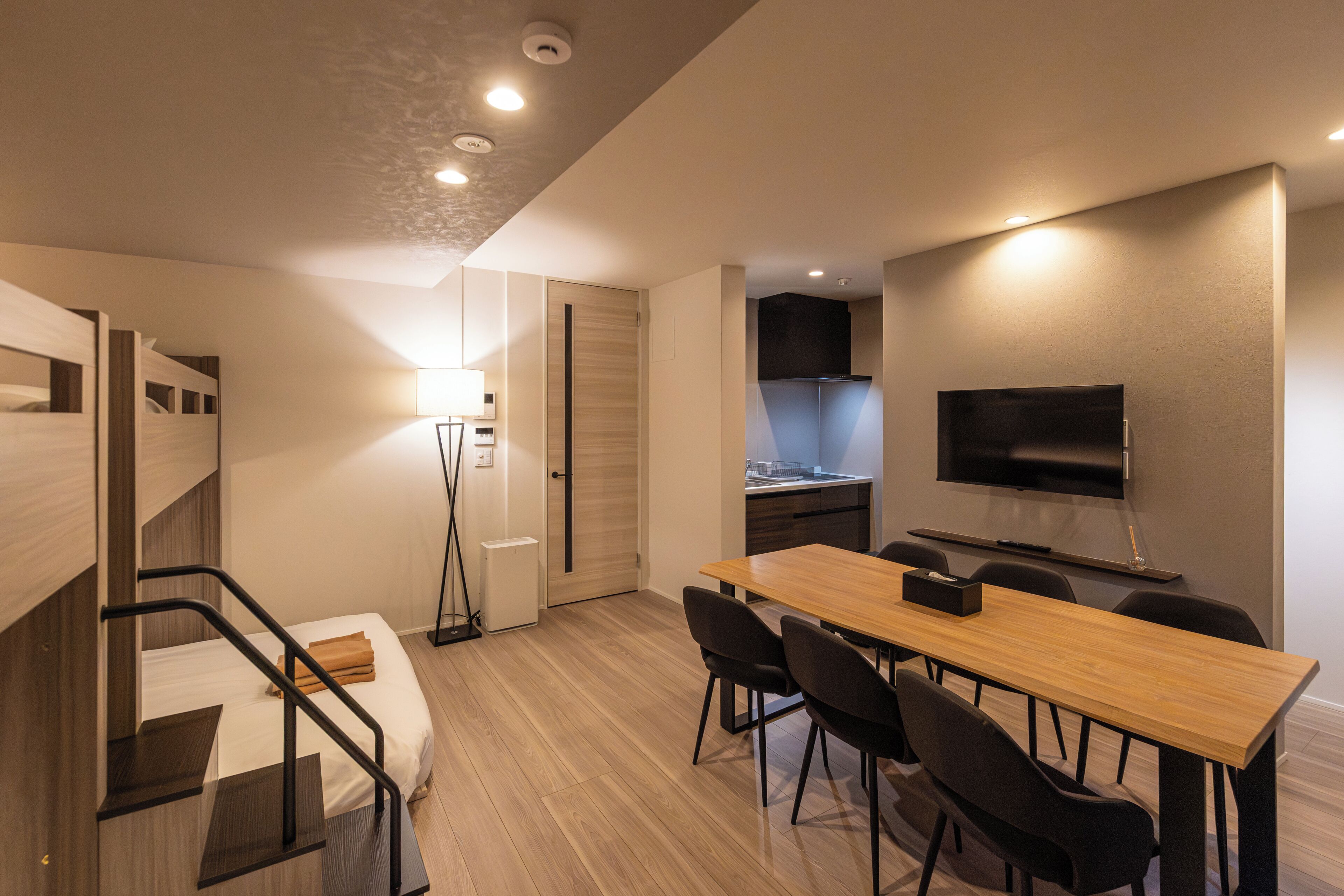 Een compacte kamer met een bed, een bureau met stoelen, een televisie en een kitchenette.