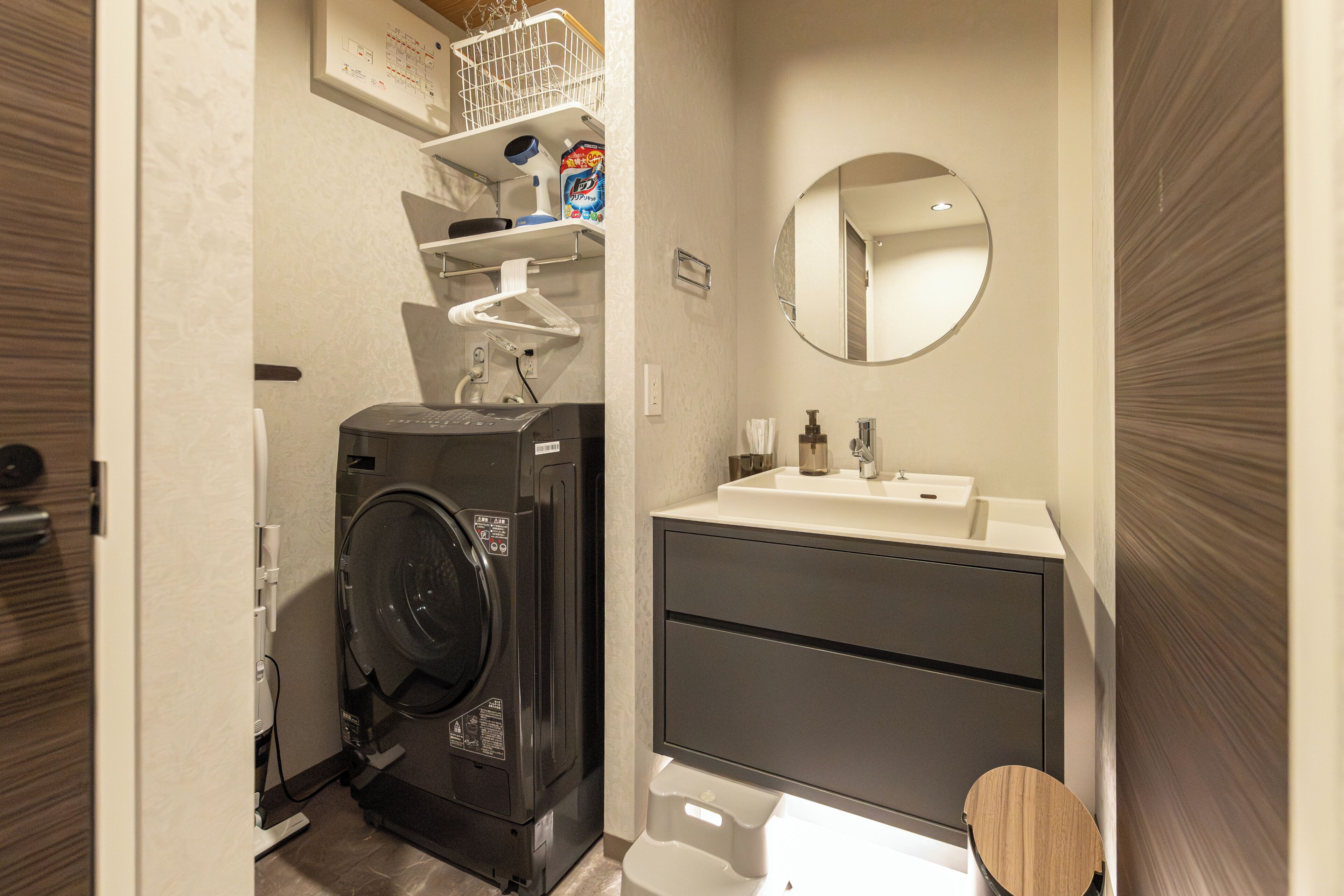 Une petite salle de bain équipée d’un lave-linge, d’un lavabo, d’un miroir et de toilettes.