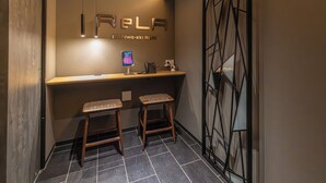 Un área de recepción con mostrador, dos taburetes, un teléfono y un cartel que dice 'RELA Koshima-eki Night'.