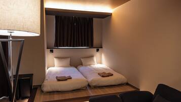 A small, modern room with two beds, a desk, and a lamp.
