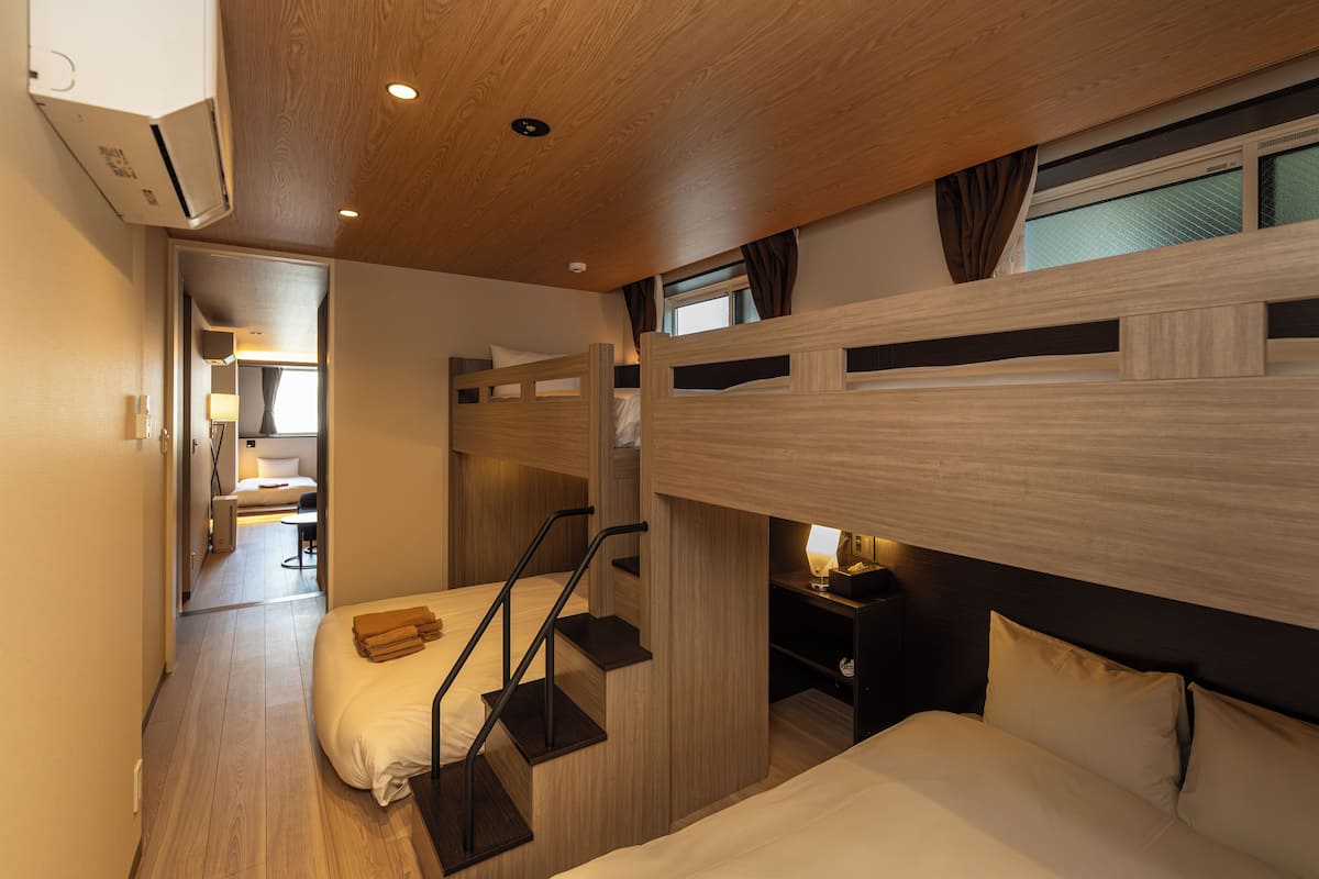 Een compacte hotelkamer met stapelbedden, een klein bureau met lamp en een raam met gordijnen.