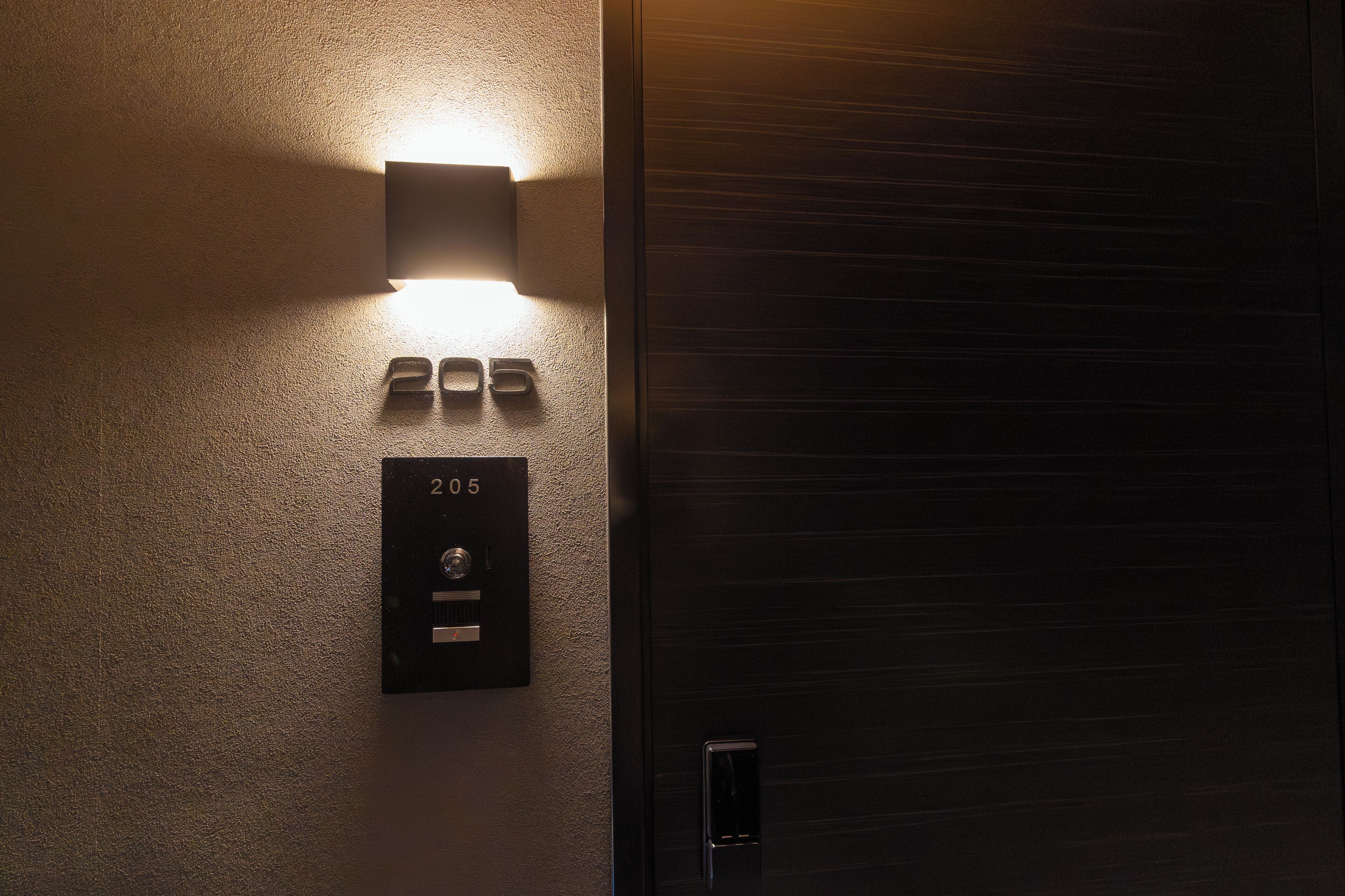 A wall-mounted light fixture, a door with a metallic handle, and a room number sign.
