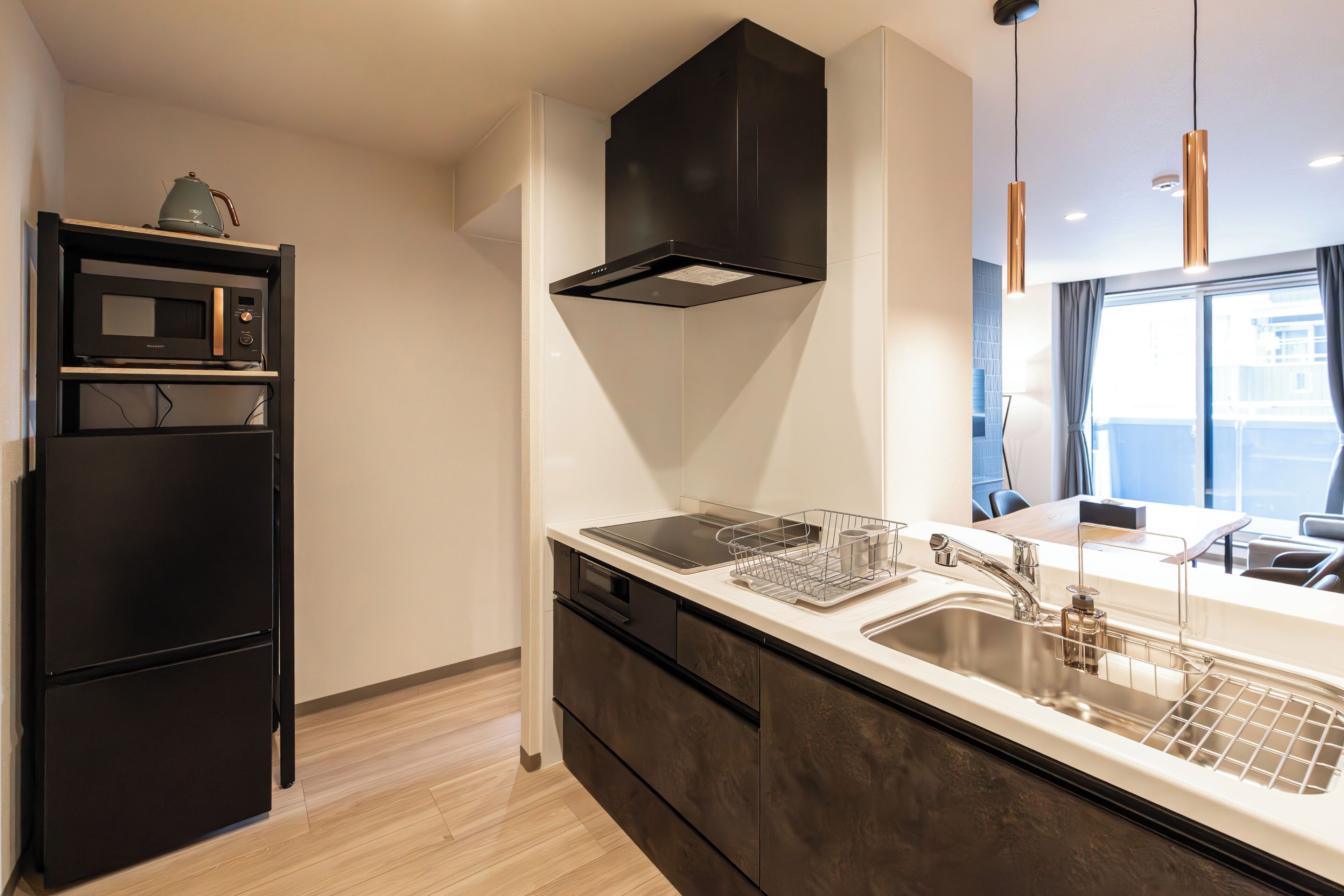 A modern kitchen with a built-in microwave, oven, and dishwasher, a stainless steel sink, and pendant lighting.