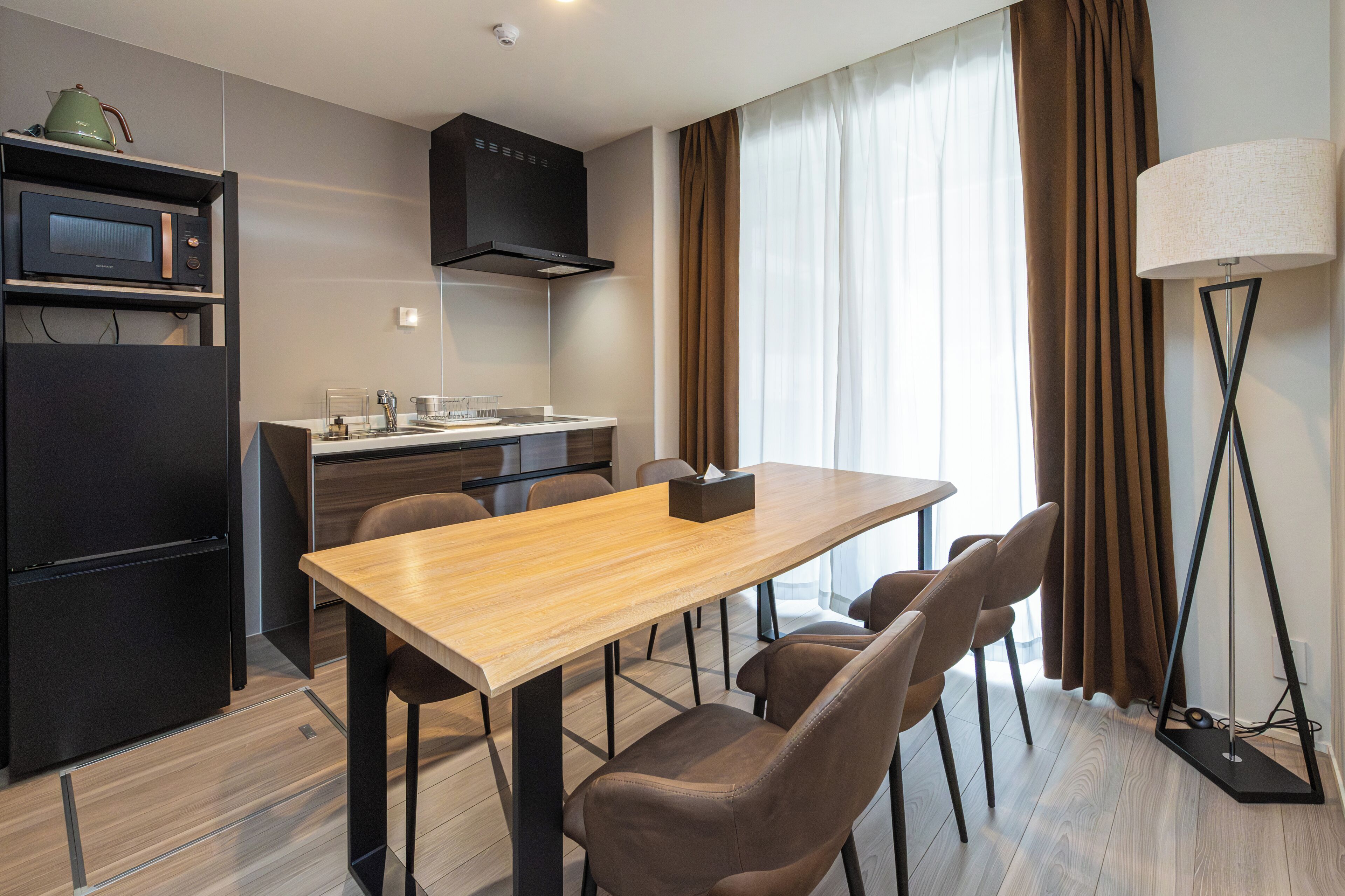 A modern kitchen with a microwave, stove, and sink, a dining table with chairs, and a floor lamp.