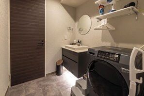 Un baño moderno con puerta de madera oscura, un lavamanos, un espejo, una lavadora y un cubo de basura pequeño.