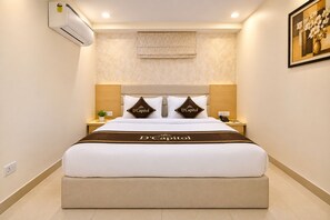 Habitación de hotel con una cama grande, dos mesitas de noche, aire acondicionado de pared, un cuadro y una ventana con cortina estampada.