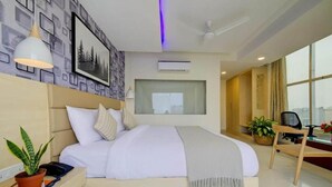Ett modernt hotellrum med en stor säng, ett skrivbord, en stol, en krukväxt och ett fönster med utsikt över staden.