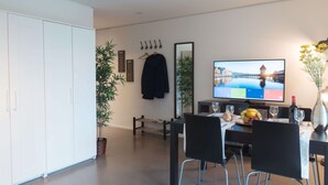 Een moderne eethoek met een televisie, stoelen, een tafel en een potplant.