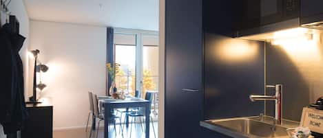 A modern kitchen with a built-in sink, a dining area with a table and chairs, and a view of the outdoors through a large window.