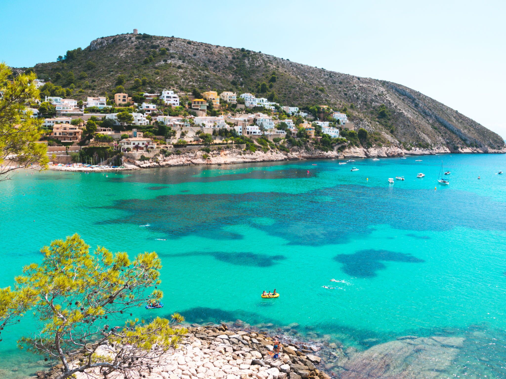 A coastal town with buildings along the shoreline, clear turquoise waters, and rocky terrain.